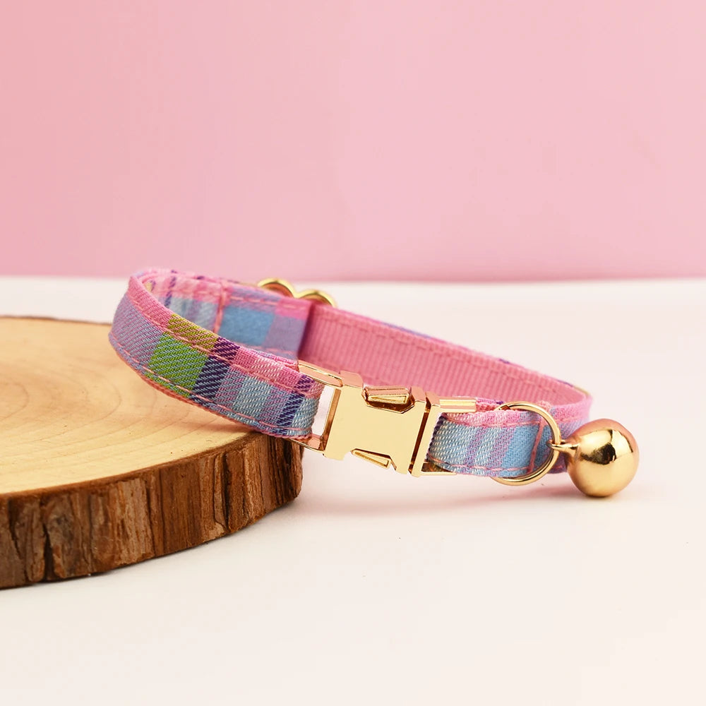 Plaid cat collar with pink band and gold clasp on a wooden block against a pink background